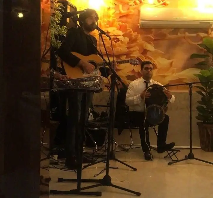 اجرای موسیقی زنده و شاد در کافه رستوران سنتی دیبا، شامل نوازنده گیتار و خواننده به همراه نوازنده تمبک در فضایی سنتی و دلپذیر.