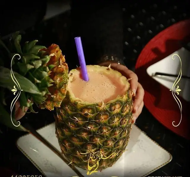 نوشیدنی خنک آناناس سرو شده درون میوه طبیعی آن با نی بنفش در کافه رستوران سنتی دیبا، انتخابی ویژه و گوارا.