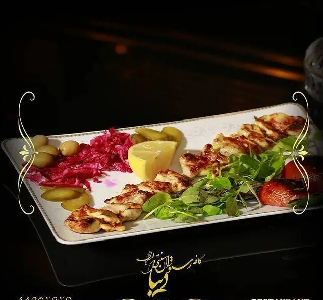 غذای خوشمزه جوجه کباب ایرانی کافه رستوران سنتی دیبا با زیتون، کلم، خیارشور، لیمو، سبزیجات معطر و گوجه کبابی.