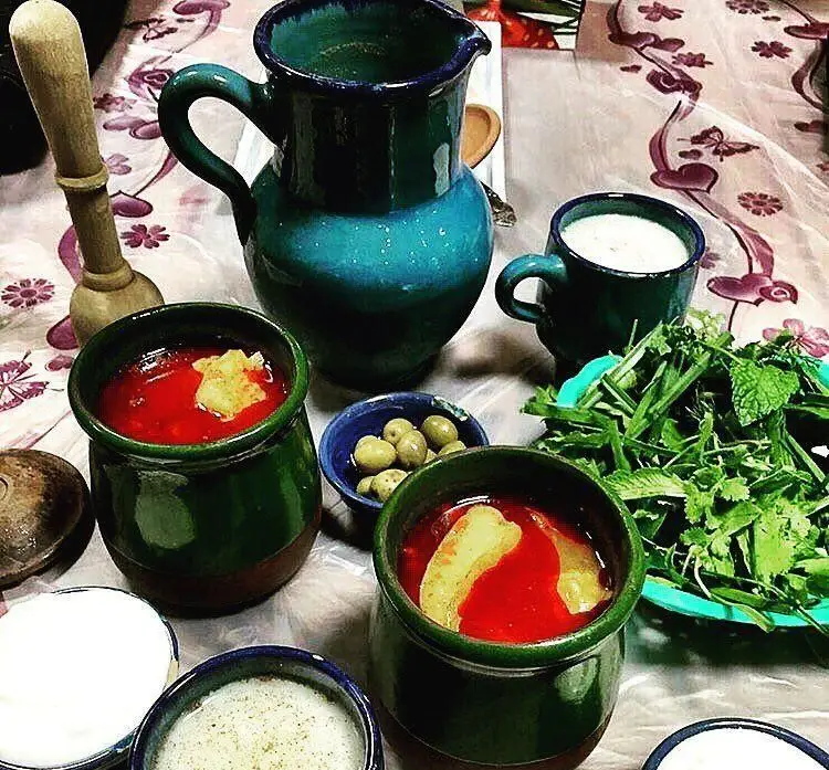 سفره اصیل ایرانی در کافه رستوران سنتی دیبا شامل کوزه دیزی، سبزی خوردن تازه و زیتون در ظروف سفالی زیبا.