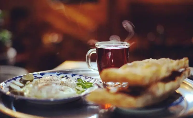 میز صبحانه گرم و دلپذیر در سفره خانه سنتی کریم خان شامل املت، چای داغ و نان تازه. لذت غذای سنتی ایرانی.