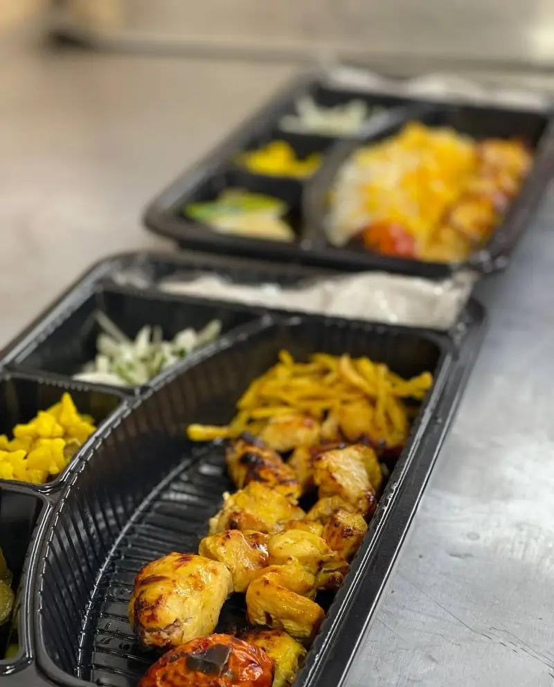 تصویر جذاب از دو پرس غذای کترینگ ته چین ناب: جوجه کباب، برنج زعفرانی، سیب زمینی و مخلفات خوشمزه در ظرف بیرون بر.