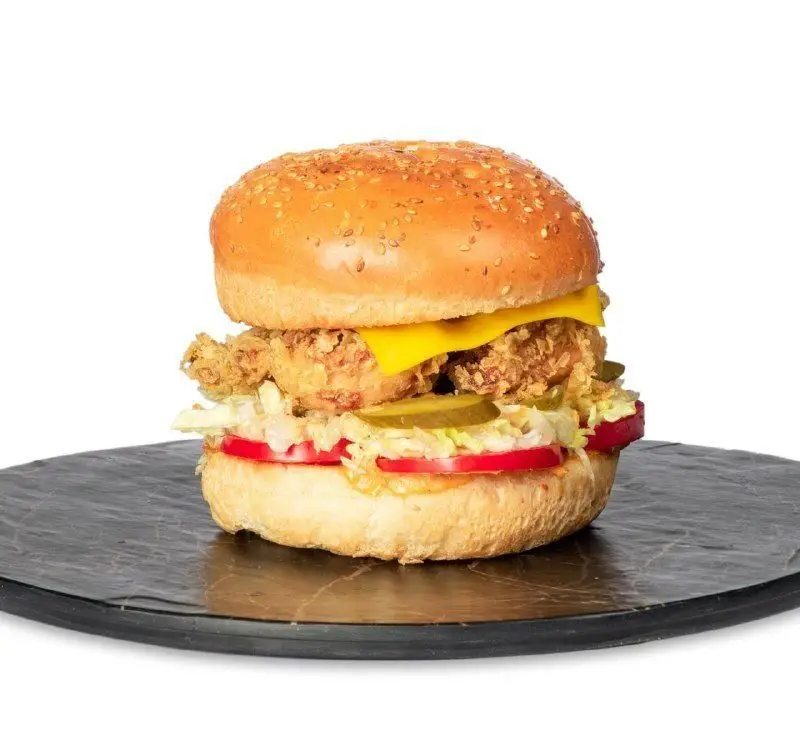 ساندویچ چیکن برگر سوخاری فست فود کامنت با نان برگر کنجدی، پنیر، کاهو، گوجه فرنگی و خیارشور، یک غذای خوشمزه.