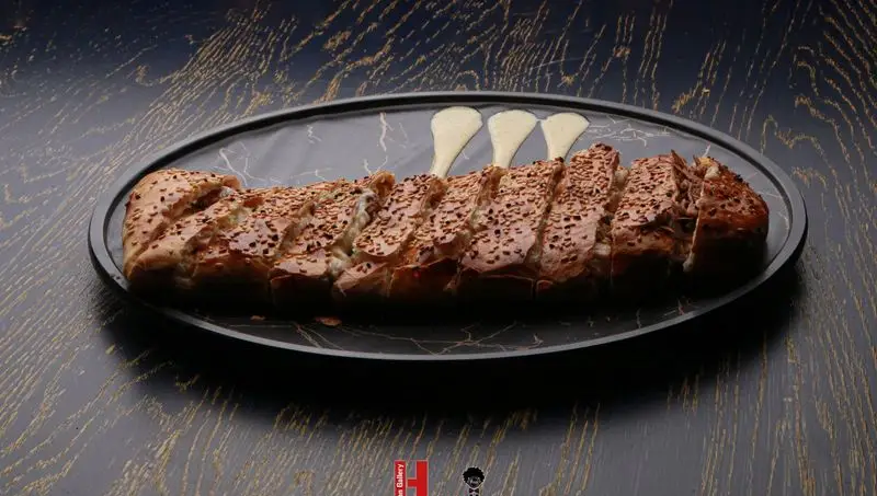 نان سیر و پنیر کنجدی تازه پخته شده آماده سرو در فست فود کامنت، بر روی سینی بیضی مشکی با سس مخصوص، غذایی لذیذ و دلپذیر.