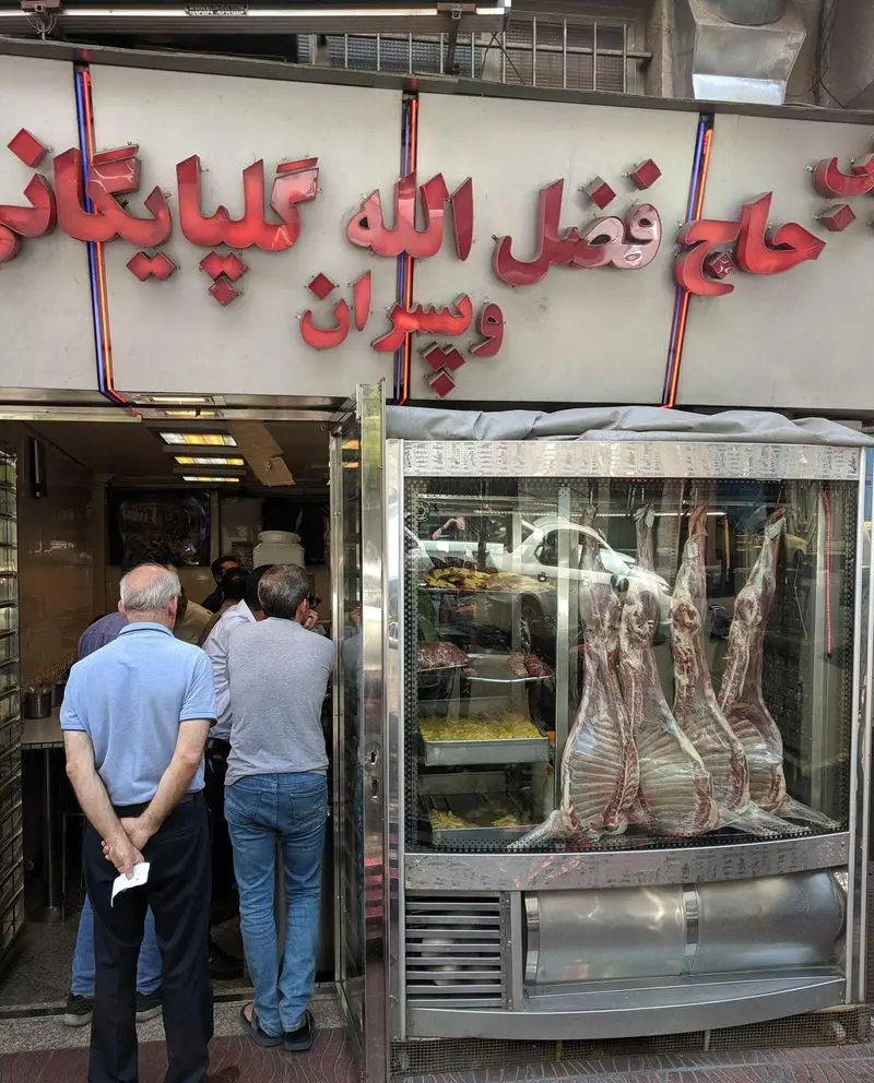 تصویری از مغازه کبابی گلپایگانی حاج فضل الله و پسران، با گوشت تازه گوسفندی آویزان در یخچال و حضور مشتریان