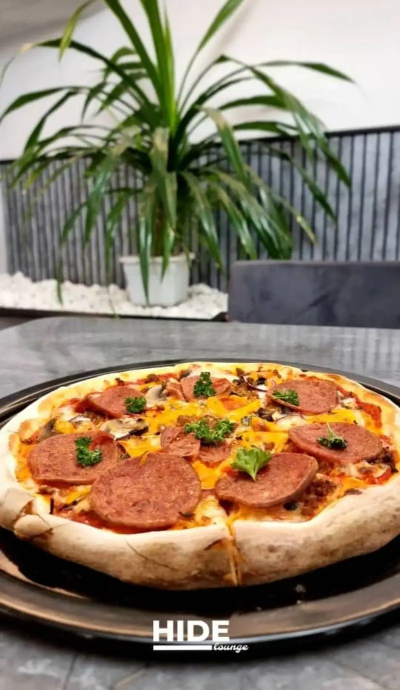 پیتزای خوشمزه و پرملات کافه رستوران هاید لانژ شامل سوسیس، قارچ و پنیر با نان ضخیم روی میز. تجربه طعمی عالی در هاید لانژ.