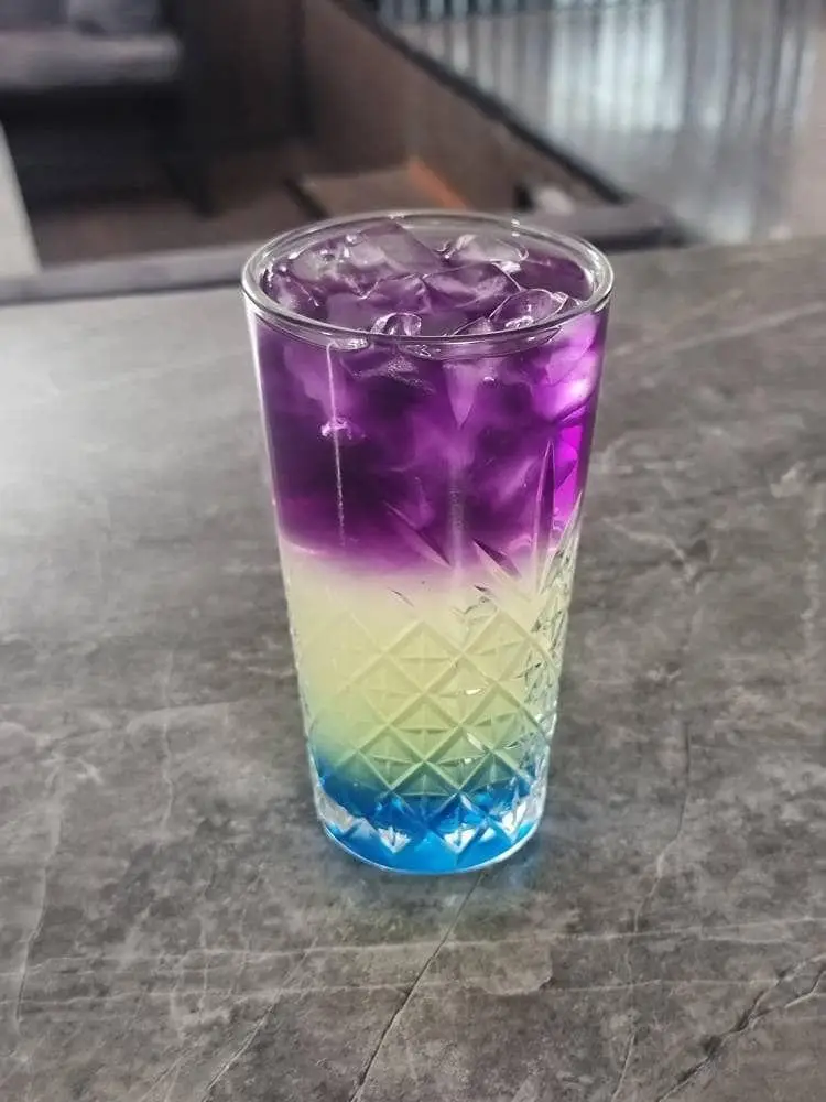 ماکتیل رنگارنگ لایه ای جذاب با رنگ های بنفش، سبز و آبی، پر از یخ در کافه رستوران هاید لانژ. انتخابی عالی از منوی نوشیدنی های ویژه.