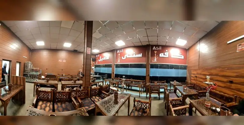 نمایی داخلی از کافه سنتی اصیل با دکوراسیون چوبی، میز و صندلی های سنتی و قلیان های آماده برای پذیرایی در فضایی دلنشین.