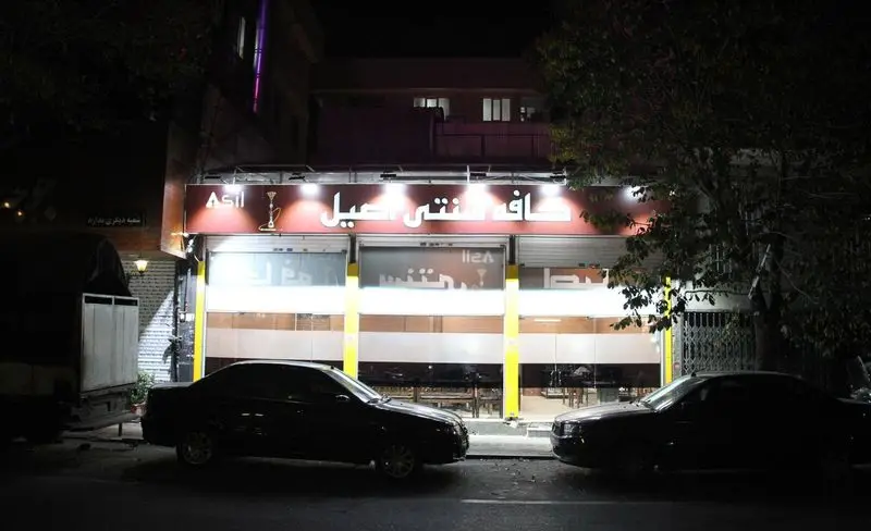 تصویری از نمای بیرونی کافه سنتی اصیل در شب با تابلوی نورانی، نشانگر قلیان و فضای آرامش‌بخش، مناسب دورهمی‌ها.