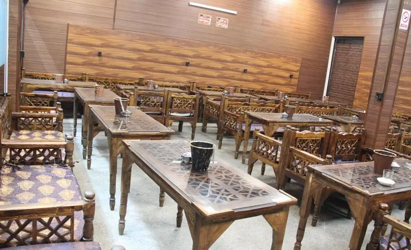 محیط داخلی کافه سنتی اصیل با میز و صندلی‌های چوبی منبت‌کاری شده و دکوراسیون گرم و سنتی، فضایی آرامش‌بخش برای مشتریان.