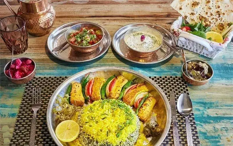 تصویری از میز غذاهای اصیل و متنوع رستوران ایرانی چارگاه شامل کباب، برنج زعفرانی، سالاد شیرازی و ماست خوشمزه.