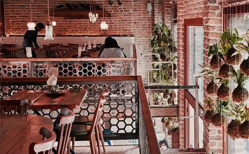 دکوراسیون داخلی زیبا و منحصر به فرد رستوران ایرانی چارگاه با میز و صندلی چوبی، دیوارهای آجری و گیاهان آویزان طبقاتی.