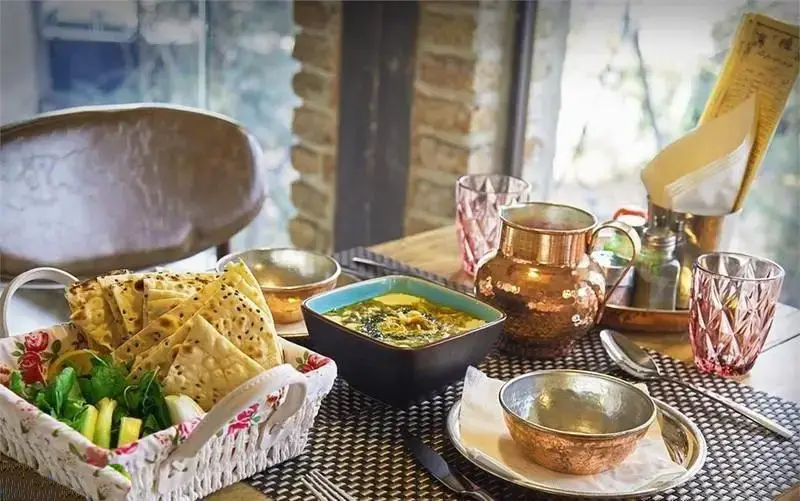 میز چیدمان شده رستوران ایرانی چارگاه با نان و سبزی تازه، آش سنتی و ظروف مسی اصیل. لذت غذای خانگی ایرانی.