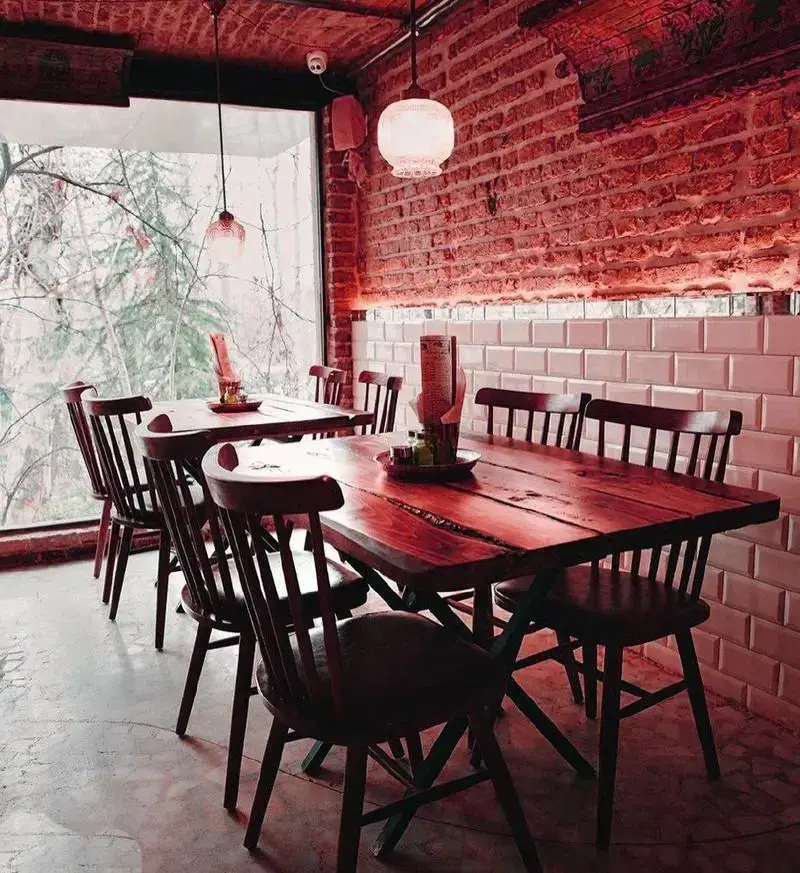 فضای داخلی دنج رستوران ایرانی چارگاه با میز و صندلی چوبی، دیوار آجری و پنجره بزرگ رو به طبیعت. تجربه‌ای دلنشین برای مشتریان.