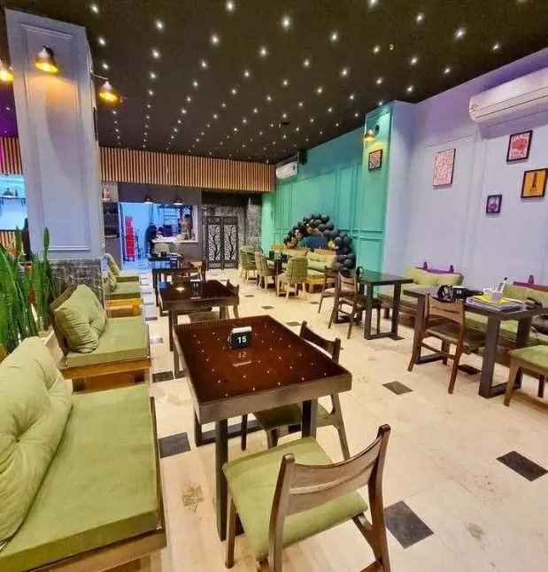 نمای داخلی شیک کافه رستوران آوا با چیدمان مبلمان سبز رنگ، میزهای چوبی تیره، سقف مدرن پرستاره و نورپردازی جذاب.
