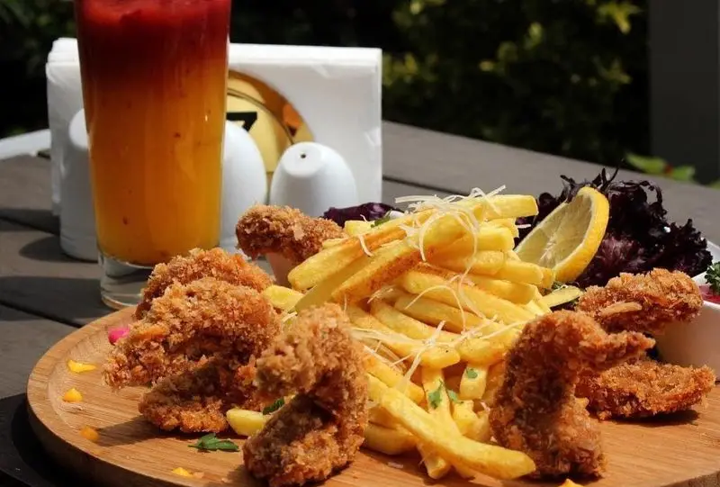 نمای نزدیک از سفارش دلپذیر کافه رستوران شاندیز گالریا: سیب زمینی سرخ کرده طلایی با پنیر، لقمه های سوخاری و نوشیدنی خنک لایه‌ای.