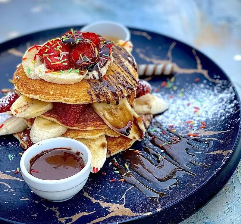 پنکیک خوشمزه کافه رستوران شاندیز گالریا با موز، توت فرنگی، سس شکلات و ترافل رنگی، انتخابی عالی برای صبحانه یا دسر.