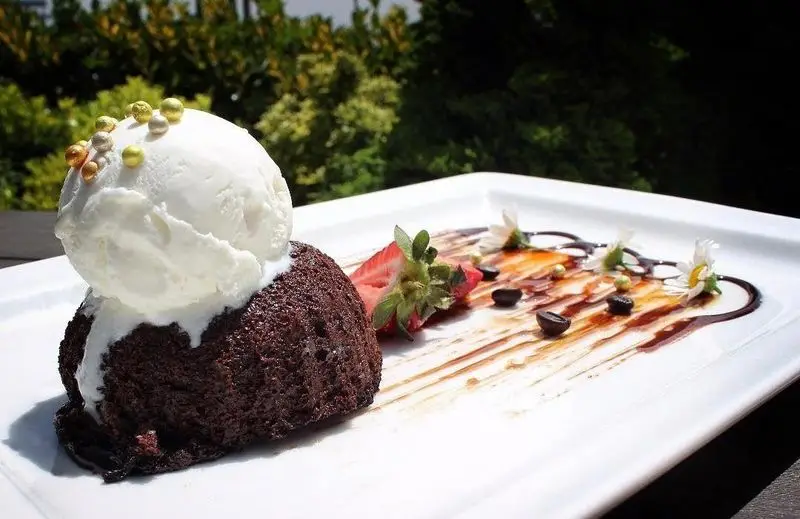 دسر ولکانو شکلاتی با بستنی وانیلی، مرواریدهای خوراکی و تزیین میوه در کافه رستوران شاندیز گالریا. تجربه طعمی لذیذ و دلنشین.