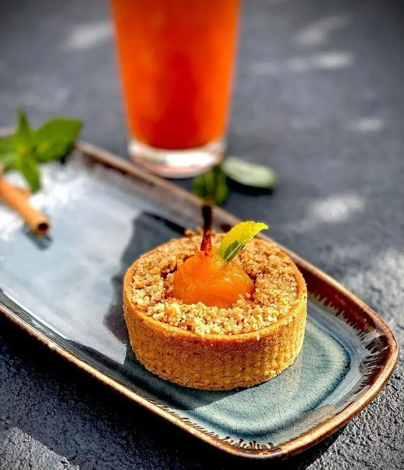 دسر لذیذ تارت میوه‌ای با کرم زردآلو و کرامبل در کافه رستوران شاندیز گالریا، همراه با نوشیدنی خنک برای لحظات دلنشین.