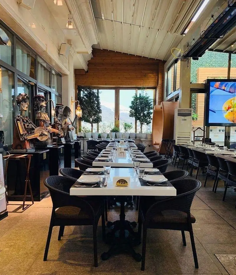 کافه رستوران شاندیز گالریا: فضای دنج و مدرن با میزهای چیدمان‌شده، دکوراسیون هنری، منظره دلنشین طبیعت برای تجربه غذایی لذت‌بخش.