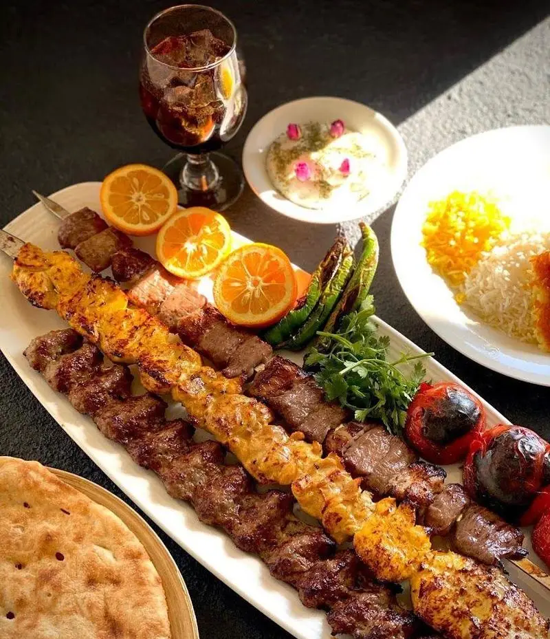 سفره‌ای پر از کباب کوبیده، جوجه کباب و برگ به همراه برنج زعفرانی، مخلفات و نوشیدنی در کافه رستوران شاندیز گالریا، تجربه غذای اصیل ایرانی.