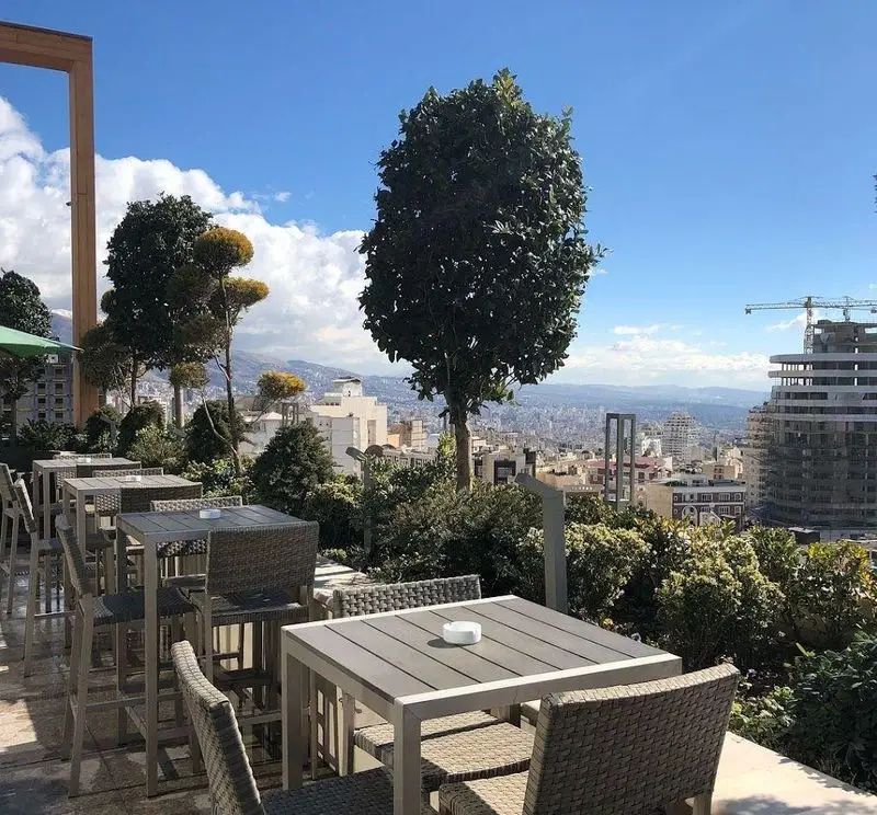 تراس روف گاردن کافه رستوران شاندیز گالریا با میز و صندلی‌های مدرن، منظره دیدنی شهر، کوهستان و آسمان آبی. مکانی آرام برای صرف غذا.