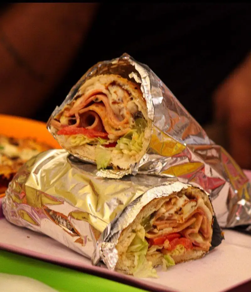 دو ساندویچ ساب لذیذ پیتزا هات، با ژامبون، پنیر، کاهو و گوجه‌فرنگی تازه، نیمه‌باز در فویل آلومینیومی، آماده لذت بردن.