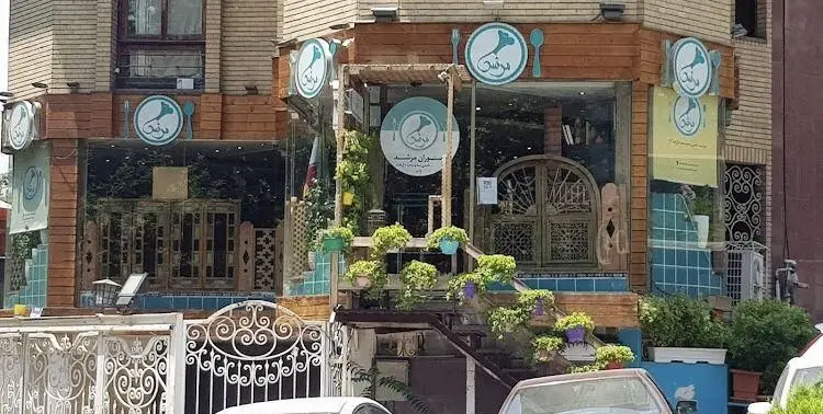 نمای بیرونی دلنشین رستوران سنتی مرشد باهنر، شامل ورودی جذاب با دکوراسیون چوبی، گیاهان سرسبز و تابلوهای "مرشد".