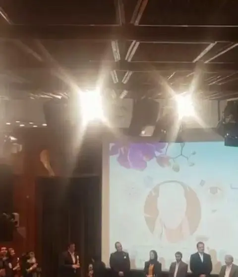تصویری از مراسم بزرگ آرایشگاه کرشمه، با حضور جمعی از متخصصین زیبایی بر روی صحنه و نمایشگر فعال در پس‌زمینه.