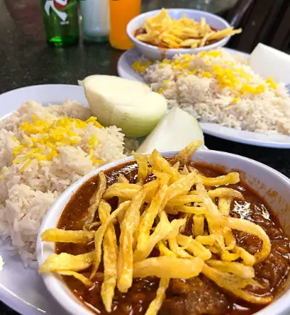 چندین پرس غذای لذیذ قیمه با برنج زعفرانی و سیب‌زمینی ترد خلالی، همراه با پیاز تازه در قیمه سرای عمو هوشنگ.