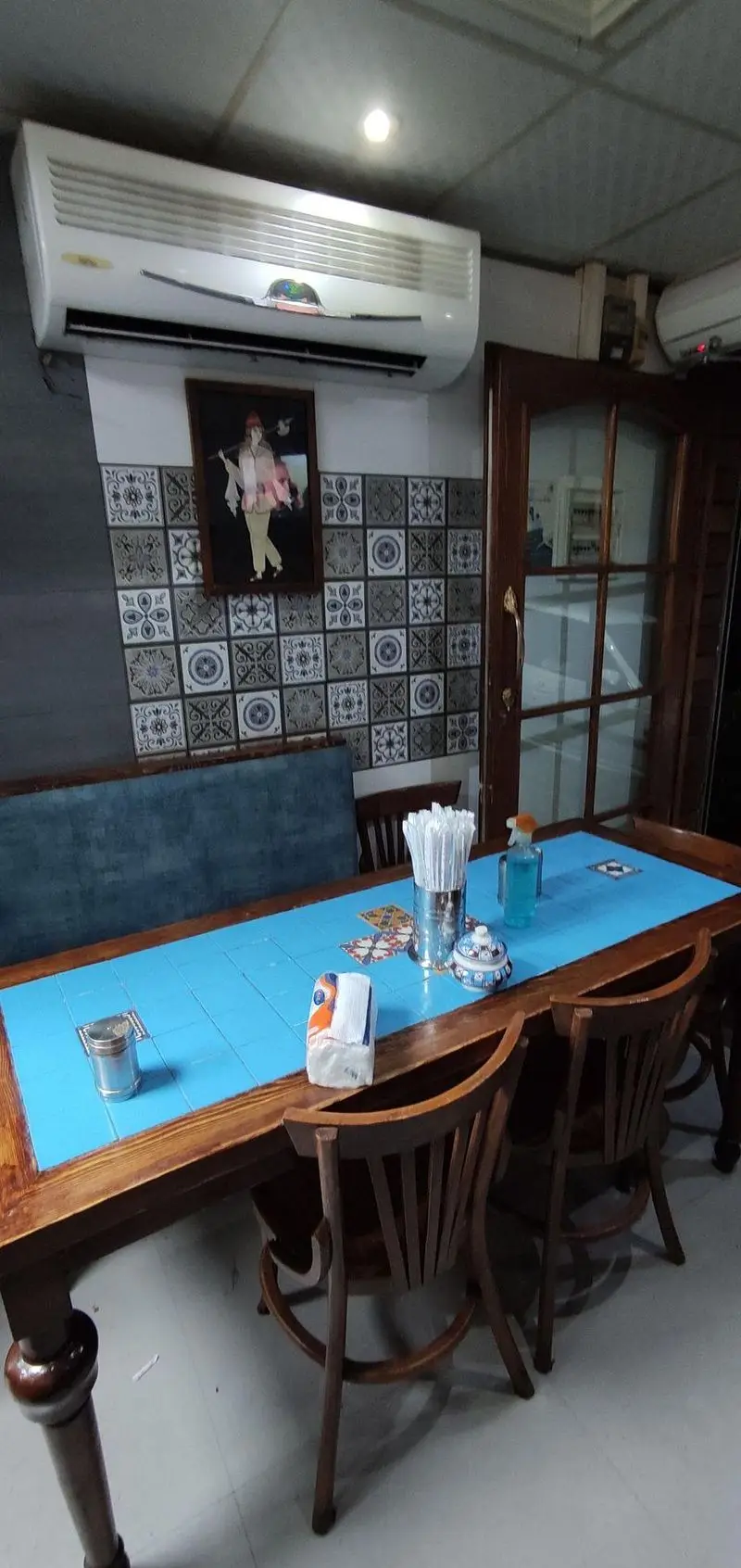 محیط داخلی قیمه سرای عمو هوشنگ، شامل میز ناهارخوری بزرگ با کاشی آبی، صندلی‌های چوبی و دکوراسیون سنتی ایرانی. مکانی دنج برای لذت از قیمه.