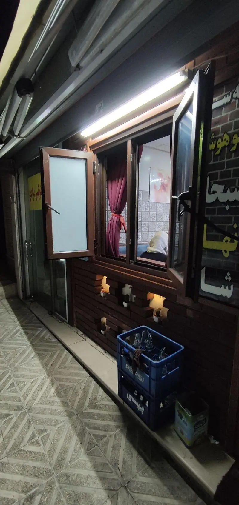 تصویری از نمای بیرونی قیمه سرای عمو هوشنگ در شب، با پنجره های باز و نورانی که فضایی سنتی و دلنشین یک رستوران را به تصویر می کشد.