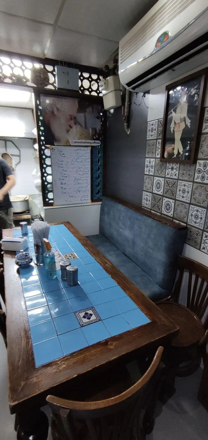 نمای داخلی قیمه سرای عمو هوشنگ با میزهای کاشی‌کاری آبی و صندلی‌های چوبی، فضایی دنج و سنتی برای لذت بردن از غذای ایرانی.