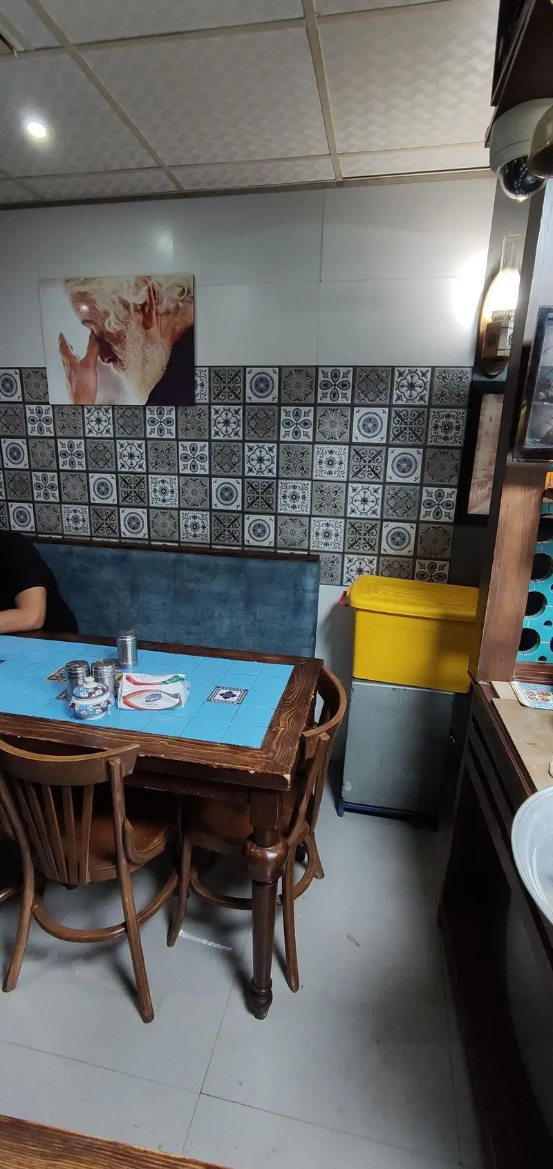 تصویری از دکوراسیون داخلی قیمه سرای عمو هوشنگ، شامل میز و صندلی چوبی، دیوار با کاشی‌های طرح‌دار سنتی و فضایی دلنشین برای سرو غذای ایرانی.