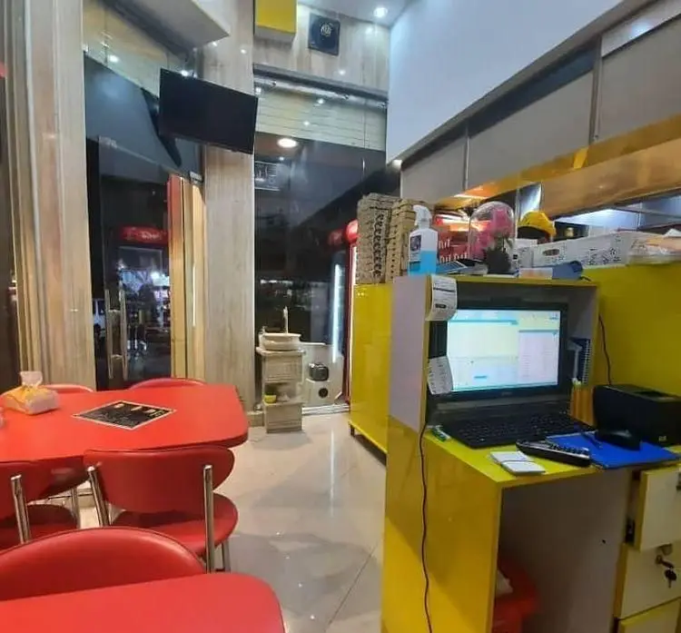 نمای داخلی فست فود سارویچ با میز و صندلی‌های قرمز، پیشخوان سفارش‌گیری زردرنگ و محیطی آماده برای پذیرایی از مشتریان.