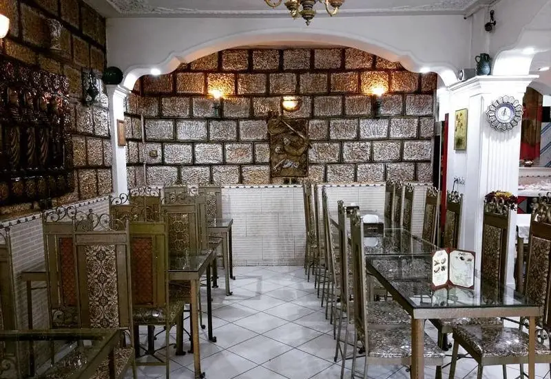 فضای داخلی مجلل رستوران طوبی با میز و صندلی‌های شیشه‌ای و فلزی، دیوارهای آجری دکوراتیو و لوستر سنتی زیبا.