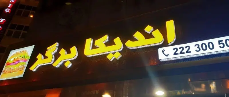 تابلوی شبانه فست فود "اندیکا برگر" با لوگوی زرد درخشان، تصویر یک برگر آبدار و شماره تلفن سفارشات: 22230050.
