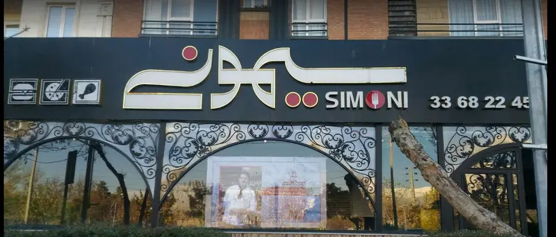 نمای بیرونی کافه رستوران سیمونی با تابلو جذاب، آیکون‌های فست فود (برگر، پیتزا، مرغ سوخاری) و شماره تماس 33682245.