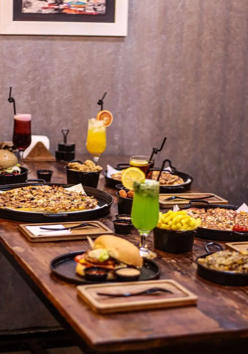 میز پربار از غذاهای کافه فست فود برج برگر شامل پیتزاهای داغ، برگرهای آبدار، سیب‌زمینی و نوشیدنی‌های گوارا.