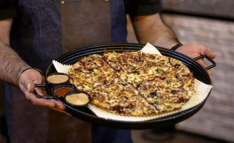 پیتزای ویژه و خوش‌منظره کافه فست فود برج برگر، آماده سرو بر روی سینی مشکی با سس‌های اشتهاآور در کنار آن.