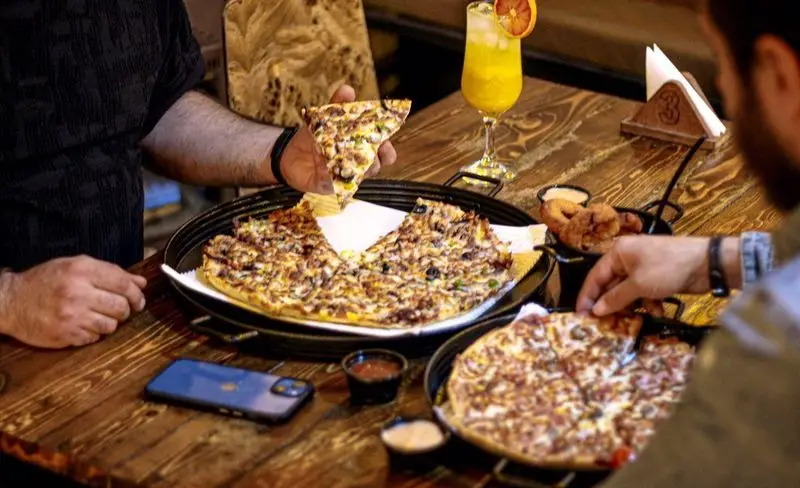 مشتریان در حال لذت بردن از پیتزا و غذاهای خوشمزه در کافه فست فود برج برگر، فضایی دلنشین برای دورهمی و تجربه طعم‌های خاص.