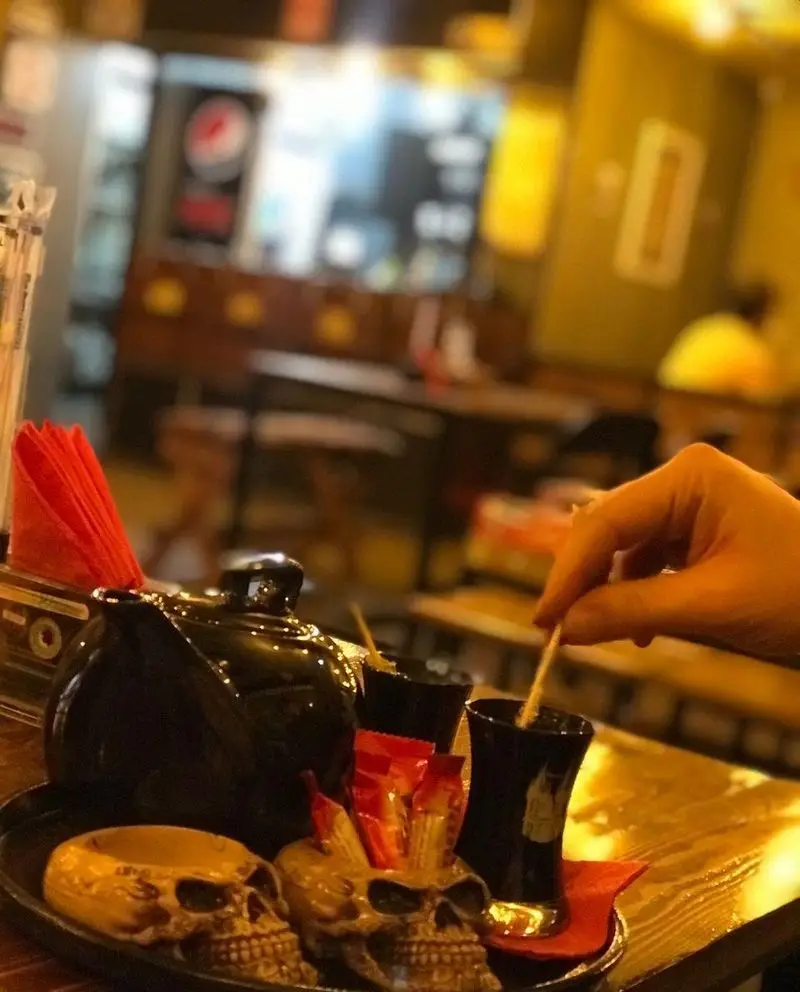 کافه فست فود برج برگر، محیطی دلپذیر برای مشتریان با سرویس خاص چای و نوشیدنی، شامل قوری و لیوان‌های شیک در کنار ظروف تزئینی اسکلتی.