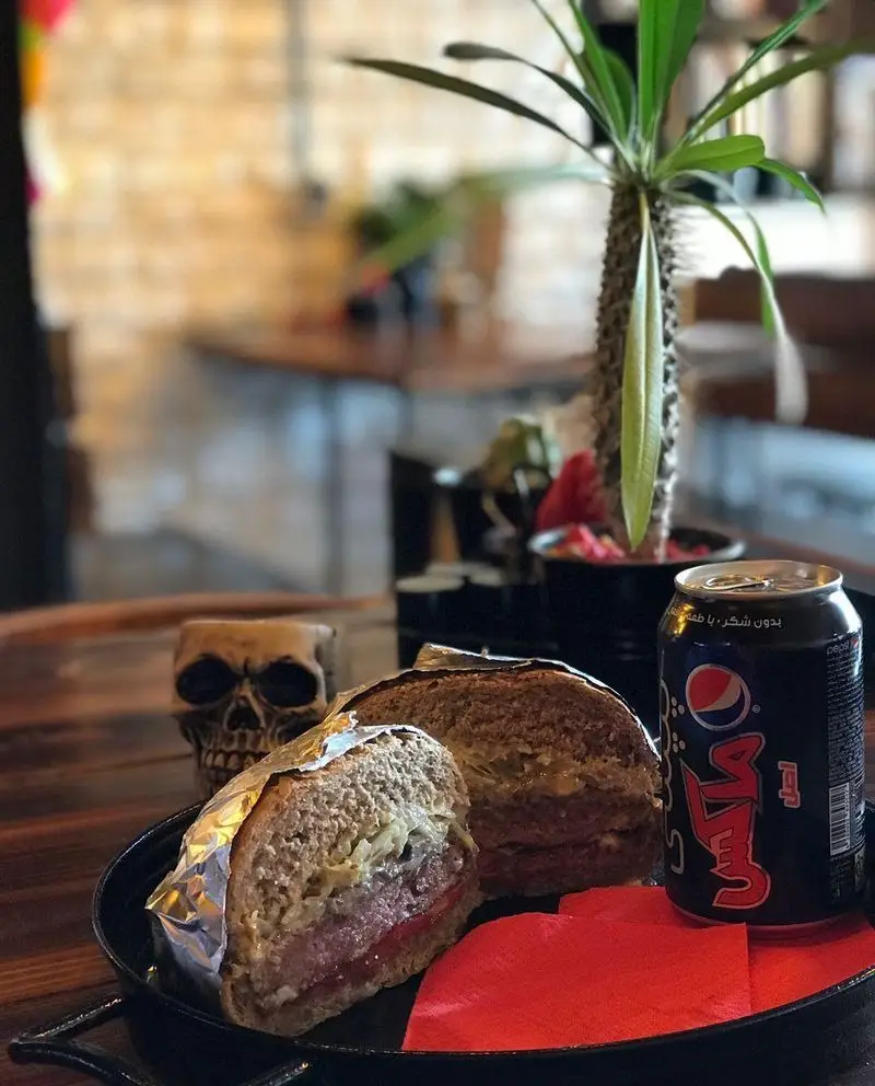 یک ساندویچ برگر ویژه و آبدار، برش‌خورده و آماده میل کردن، همراه با نوشابه پپسی، در فضای دلپذیر کافه فست فود برج برگر.