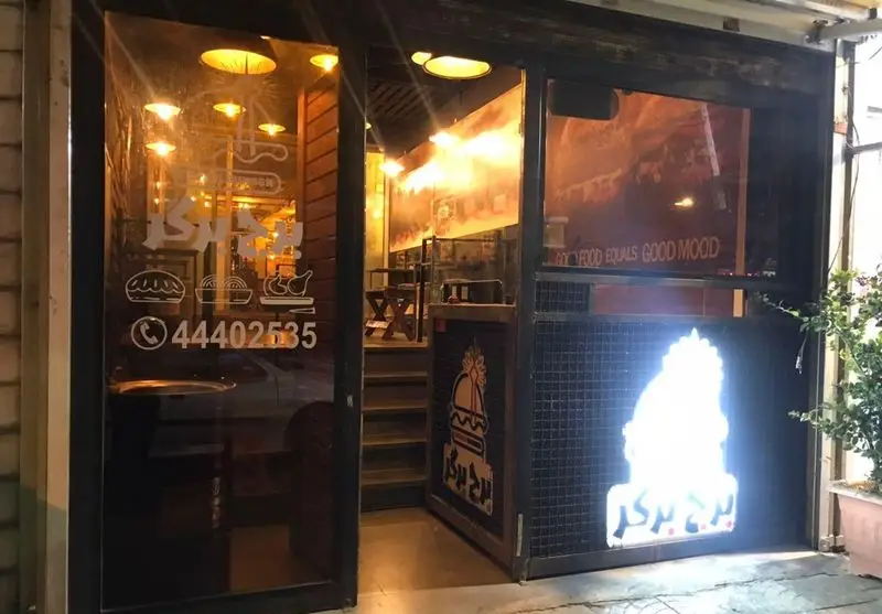 ورودی جذاب کافه فست فود برج برگر در شب، با نورپردازی دلنشین، لوگوی شاخص و شماره تماس ۴۴۴۰۲۵۳۵ جهت انواع سفارشات فست‌فود.