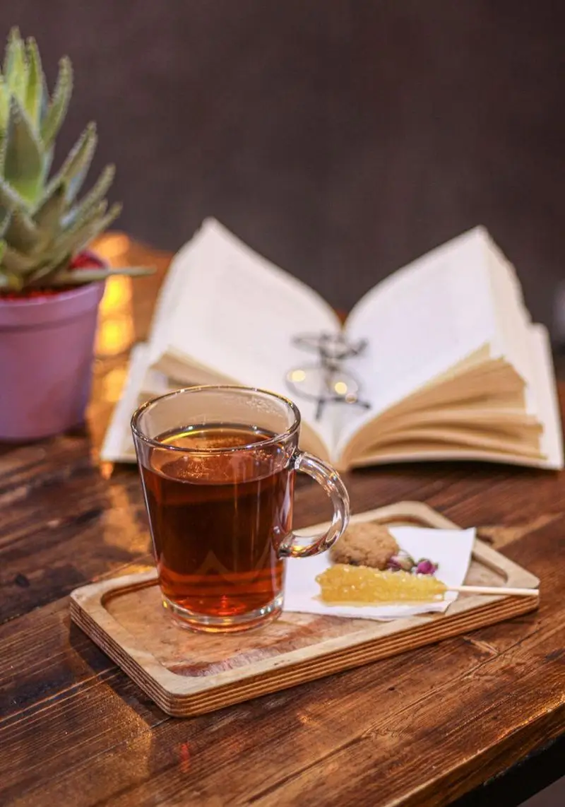 یک فنجان چای داغ با نبات و کوکی در محیط دنج کافه فست فود برج برگر، مناسب برای مطالعه و لذت بردن از لحظات آرام.