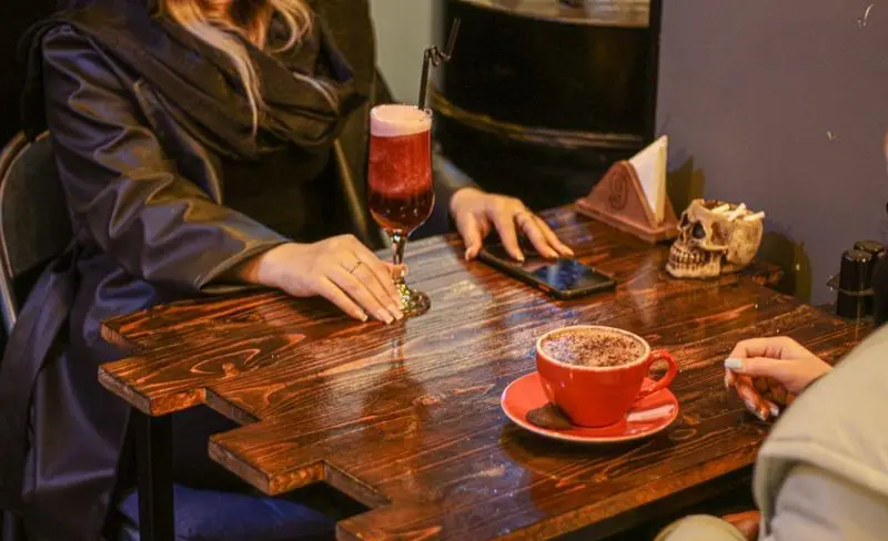 تصویری از میز کافه فست فود برج برگر با نوشیدنی قرمز، فنجان قهوه، موبایل و اسکلت تزیینی؛ فضایی دلنشین برای مشتریان.