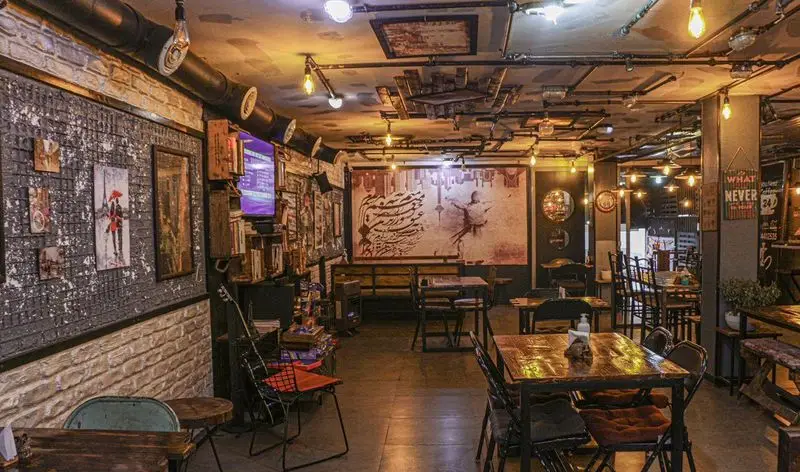 فضای داخلی کافه فست فود برج برگر با دکوراسیون صنعتی خاص، میزهای چوبی و نورپردازی گرم، محیطی دنج و هنری برای تجربه غذایی دلپذیر.