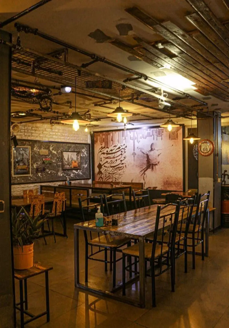فضای داخلی کافه فست فود برج برگر با دکوراسیون صنعتی و شیک، میز و صندلی‌های چوبی و فلزی، نورپردازی گرم و دیوارنگاره‌های خاص.