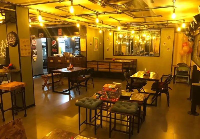 فضای داخلی مدرن و دنج کافه فست فود برج برگر با دکوراسیون جذاب صنعتی، نورپردازی گرم، میز و صندلی‌های متنوع و بازی‌های رومیزی برای اوقات فراغت.