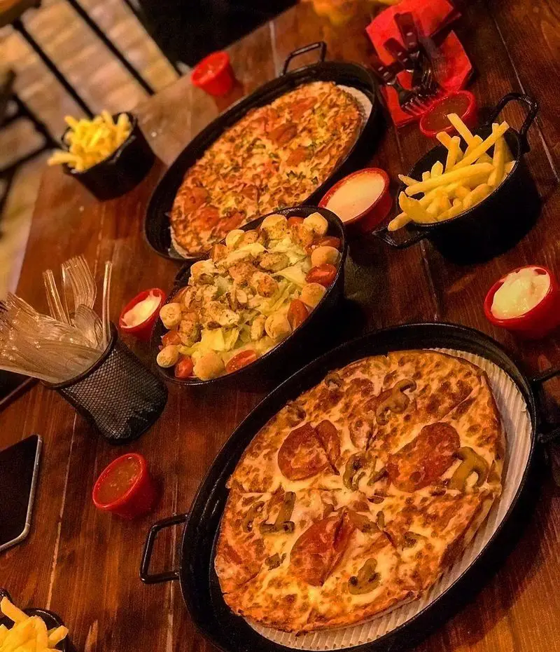 پیتزاهای پپرونی و قارچ، سالاد سزار با مرغ و نان، سیب‌زمینی سرخ‌کرده و سس‌های متنوع در کافه فست فود برج برگر.